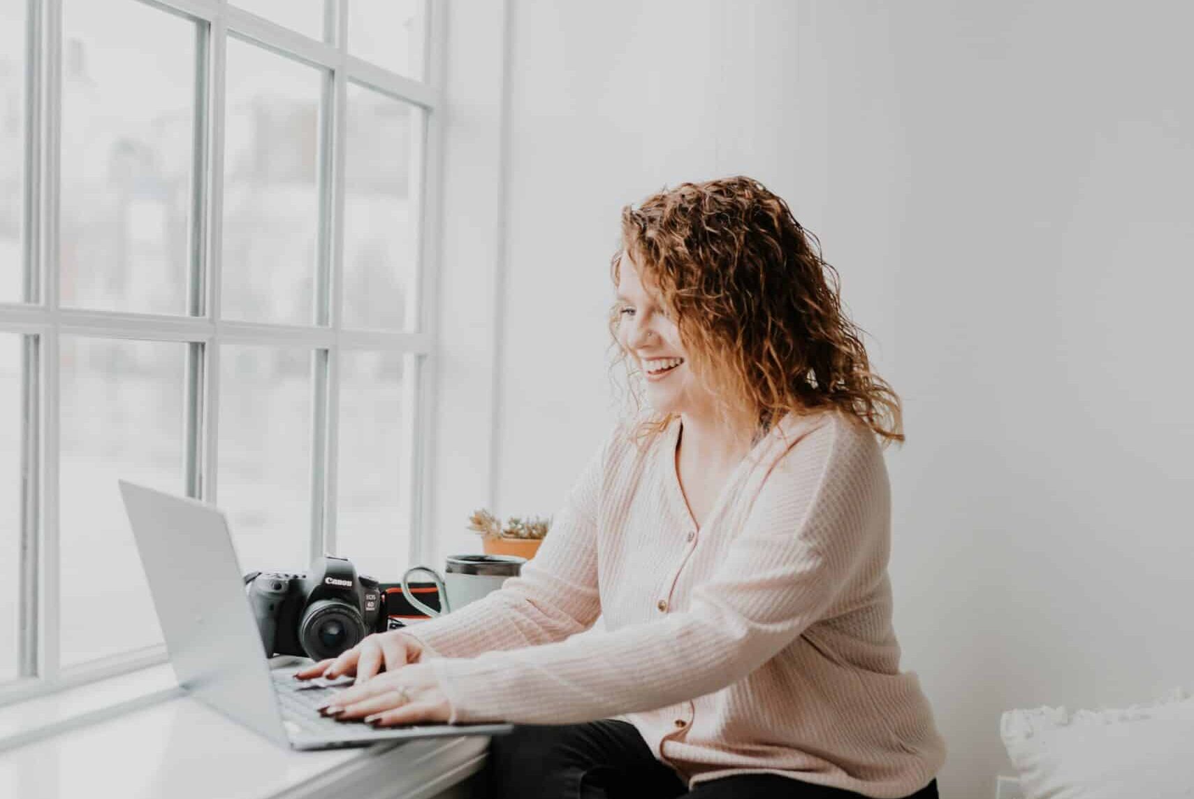 female photographer working on laptop by window