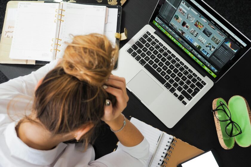 Stressed woman Sitting in Front of Macbook editing photos with her head in her hands.