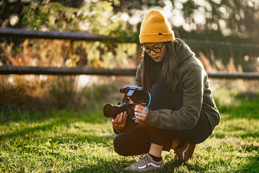 What's New for Zenfolio Video Hosting. Image of female videographer crouched low to ground with her camera, capturing a scene outdoors.