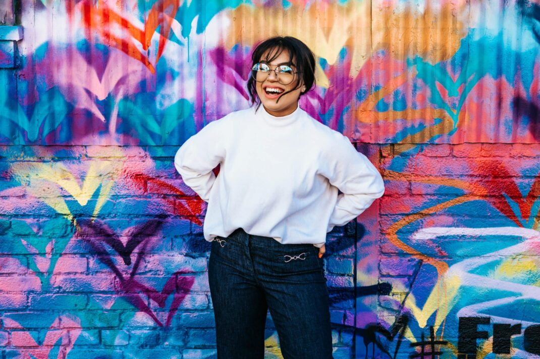woman in white shirt and jeans standing in front of multicolored graffiti wall